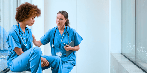 Two female doctors wearing blue scrubs stressed in a stairway. 