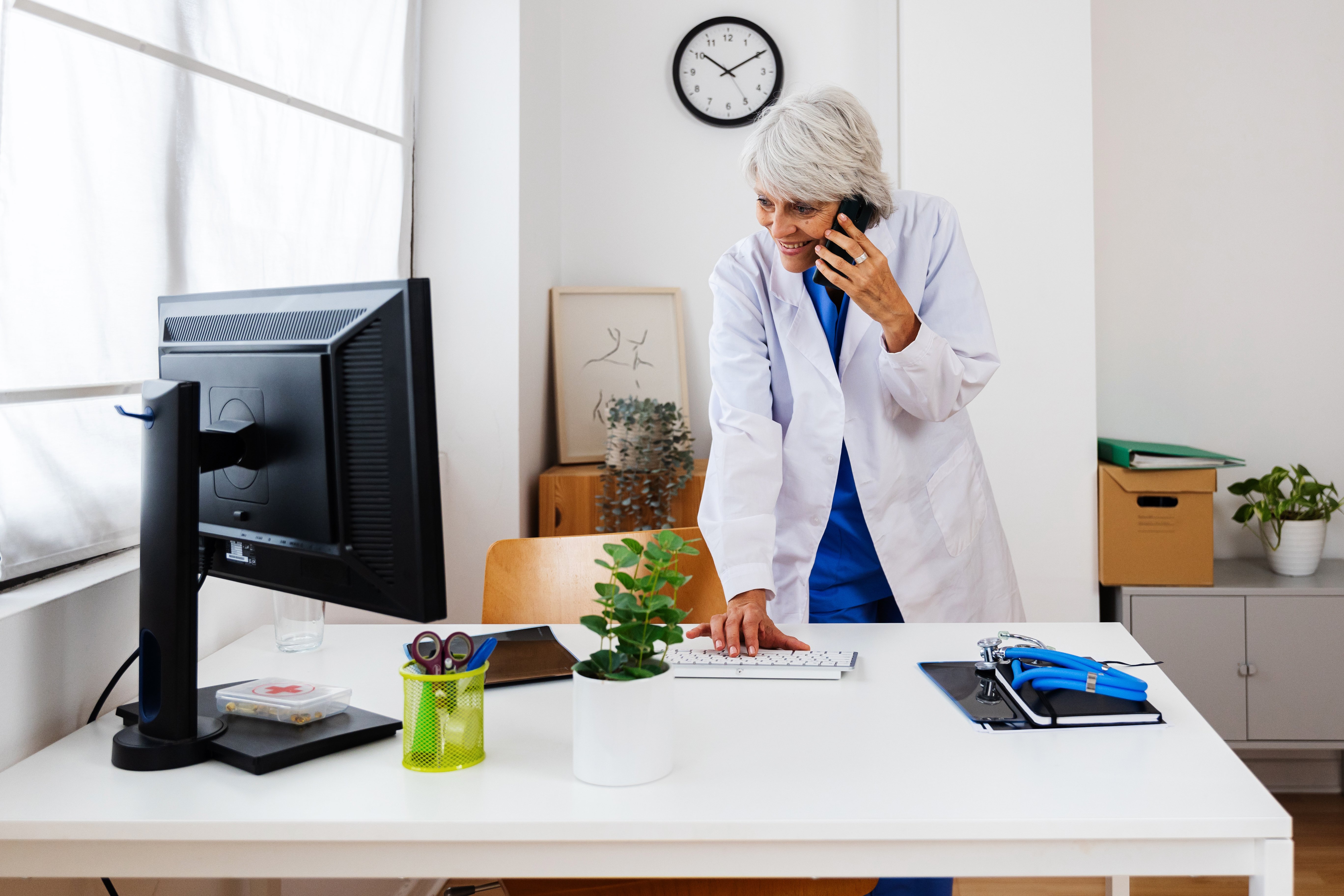 Clinician standing at computer on the phone with a patient reviewing medical history in an EHR system.
